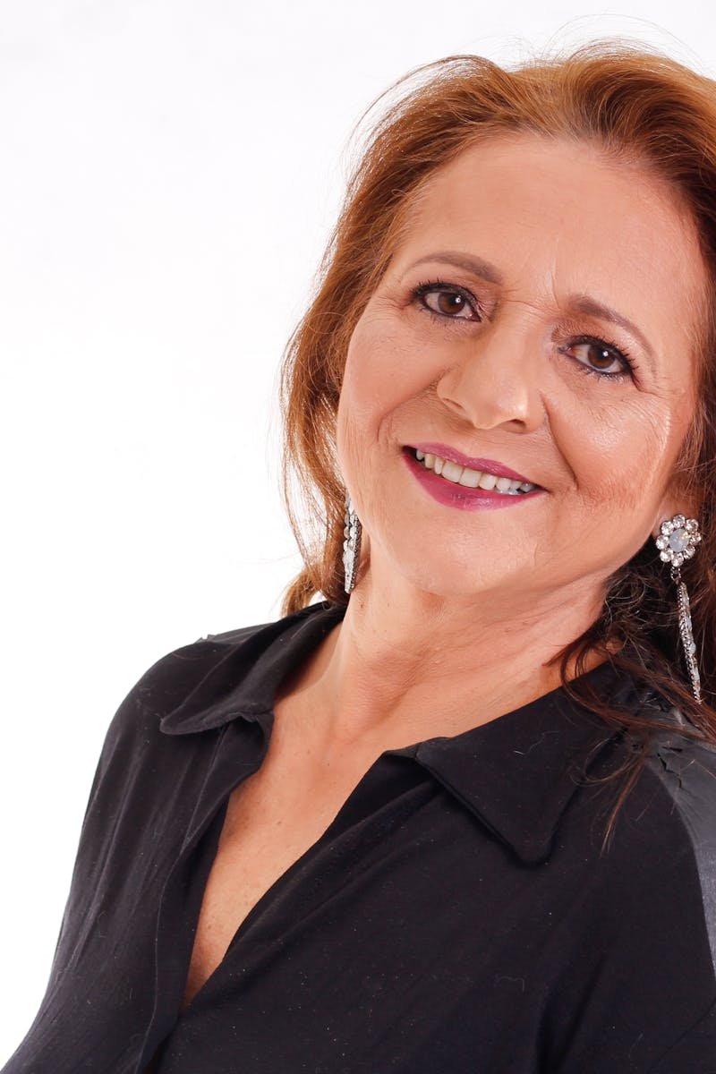 Portrait of a smiling senior woman with long hair and earrings in a black outfit.